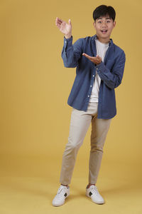 Full length portrait of boy standing against yellow background