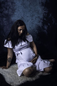 Young woman looking down while sitting against wall