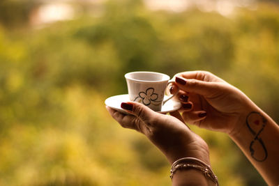 Cropped hands of woman holding coffee cup outdoors