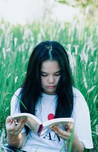 Beautiful young woman holding book against plants