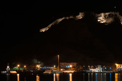 Illuminated city by sea against sky at night