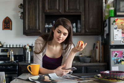Woman reading newspaper while having breakfast at table in kitchen