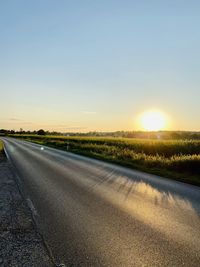 Road amidst field against sky during sunset