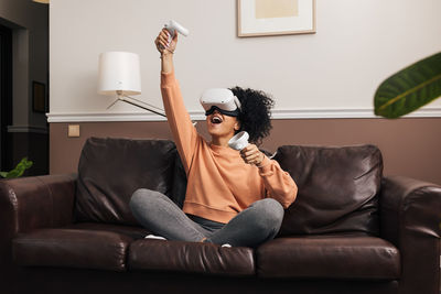 Laughing woman playing video game while sitting on sofa at home