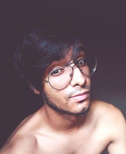 Close-up portrait of shirtless man wearing eyeglasses against wall