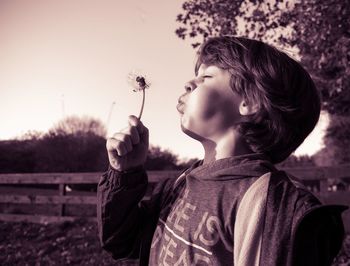 Boy with eyes closed blowing while holding dandelion