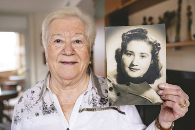 Portrait of senior woman showing an old picture of herself