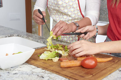 Midsection of mother and daughter preparing salad in kitchen at home