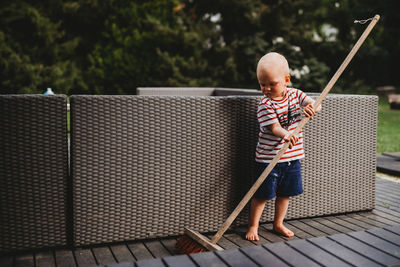 Young male child barefoot sweeping backyard patio with big broom