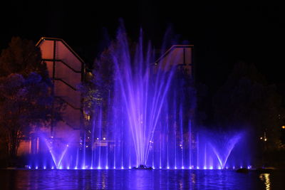 Illuminated fountain by river against sky at night