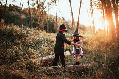 Girl wearing witch hat standing with brother at forest during halloween