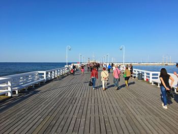 People walking on footbridge against clear blue sky