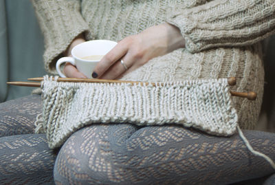 Midsection of woman having coffee while knitting wool at home