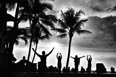 Silhouette people by palm trees against sky