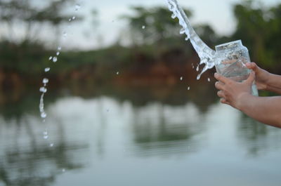 Cropped hands splashing water from jar by lake