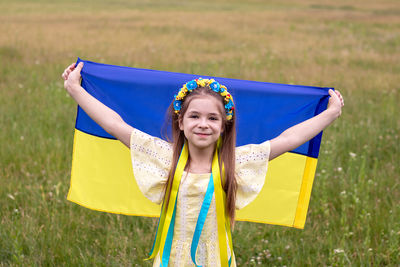 A girl in a wreath of yellow and blue flowers holds the flag of ukraine in her hands against 