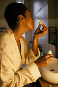 Side view of young woman applying beauty product on face