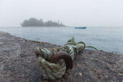 Close-up of rope on rock by sea against sky