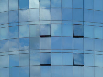 Low angle view of modern building with open windows against blue sky