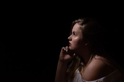 Side view of thoughtful woman looking away against black background