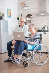 Disabled woman on wheelchair using laptop by man at home