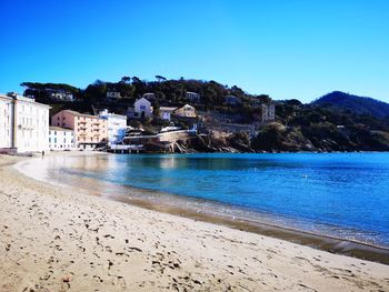 Scenic view of sea by buildings against clear blue sky