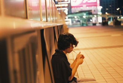 Side view of man smoking while sitting on footpath