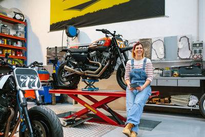 Mechanic woman holding digital tablet sitting over platform