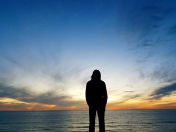 Rear view of silhouette man standing at beach during sunset