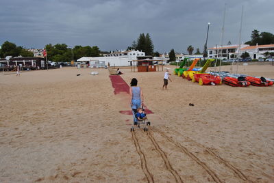 Rear view of mother pulling carriage with son at sandy beach