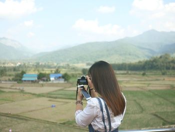 Woman photographing on field against sky