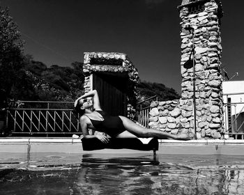 Full length of young woman lying down by swimming pool against sky