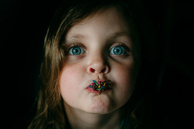 Close-up portrait of cute girl eating sweet food on black background