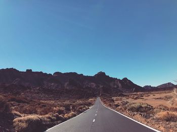 Empty road amidst landscape against clear blue sky