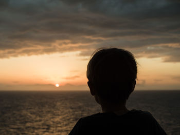 Rear view of a boy overlooking calm sea at sunset