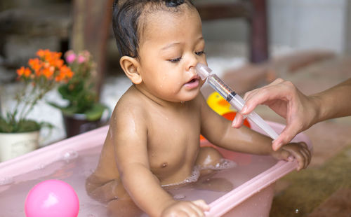 Cropped hand of woman cleaning baby nose using syringe at home