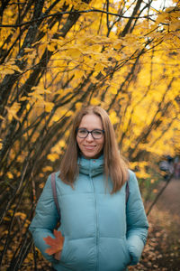 Portrait of smiling young woman standing by tree during autumn