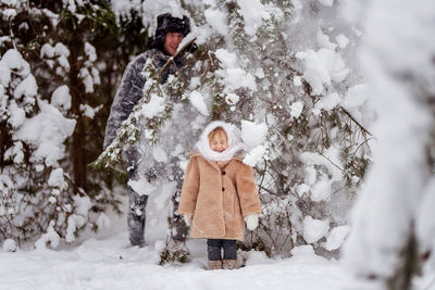 Cute smiling girl with father standing amidst snow during winter