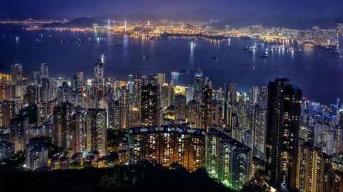 High angle view of illuminated modern buildings by lake in city at night