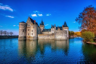 Historic building by lake against blue sky