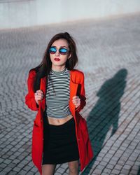 Woman in red jacket and sunglasses standing on footpath