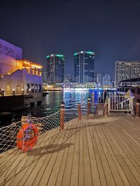 Illuminated pier by river against buildings in city at night