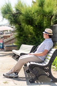 Young caucasian man in the hat sitting on bench in the park or in the sea port. yalta 2021