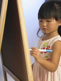 Cute girl drawing on easel by wall
