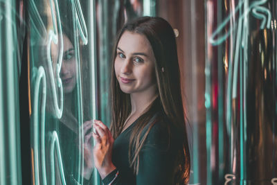 Portrait of smiling young woman by glass window with reflection