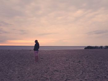 Rear view of woman walking on beach against sky during sunset