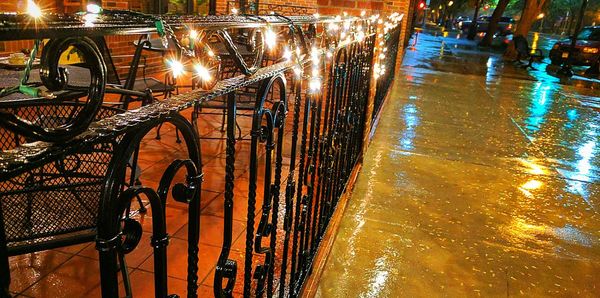 Wet illuminated bridge in city against sky at night