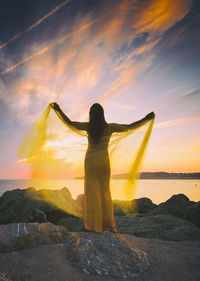 Woman in a yellow dress and cape observing a magnificent sunrise on the french basque coast vi