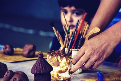 Cropped hands holding paint brushes on table with cute boy in background