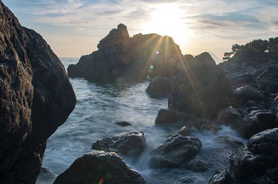 Rocks in sea against sky during sunset